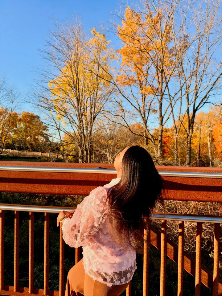 Frida from behind at a rust-red railing, looking up at yellow autumn trees