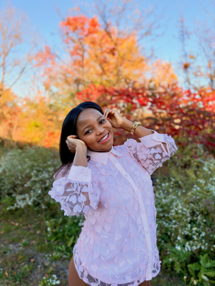 Frida smiling with her hands in her hair, in a pink lace shirt among autumn leaves