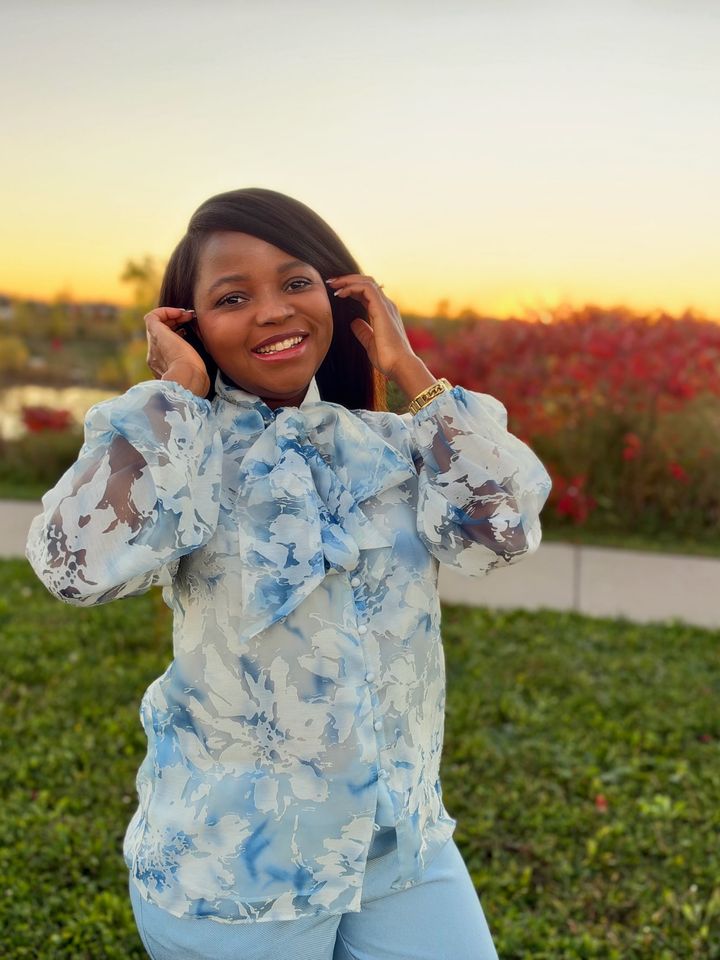 Frida in a blue floral blouse, smiling at sunset beside red bushes